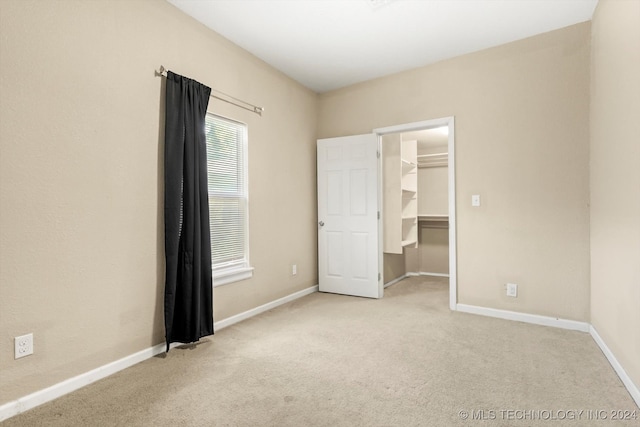 unfurnished bedroom featuring a spacious closet, a closet, and light colored carpet