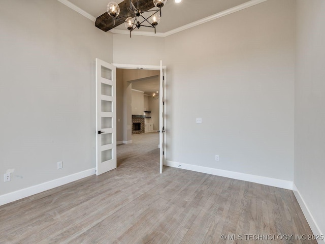 empty room featuring an inviting chandelier, ornamental molding, a fireplace, and light wood-type flooring