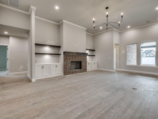 unfurnished living room featuring crown molding, a fireplace, light hardwood / wood-style flooring, and a notable chandelier