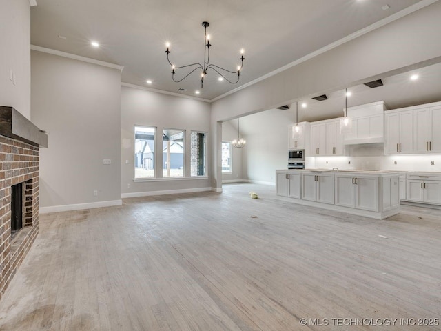 unfurnished living room with ornamental molding, light wood-type flooring, a notable chandelier, and a fireplace