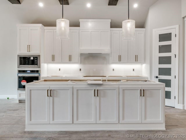 kitchen featuring a kitchen island with sink, decorative light fixtures, oven, and white cabinets