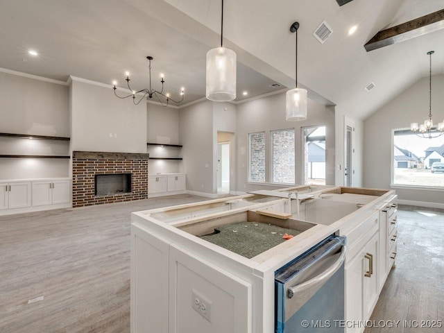 kitchen with a brick fireplace, hanging light fixtures, a center island with sink, stainless steel dishwasher, and white cabinets