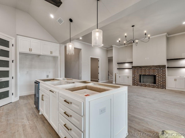 kitchen with a fireplace, decorative light fixtures, white cabinets, a center island, and light hardwood / wood-style flooring