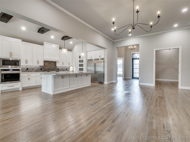 kitchen with tasteful backsplash, crown molding, open floor plan, built in appliances, and an inviting chandelier