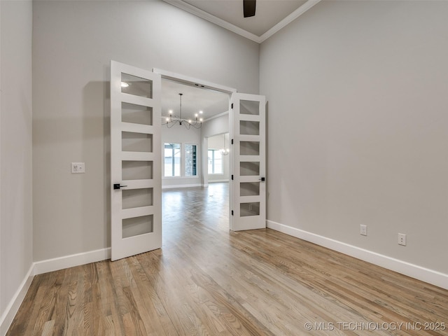 spare room featuring a notable chandelier, baseboards, crown molding, and wood finished floors
