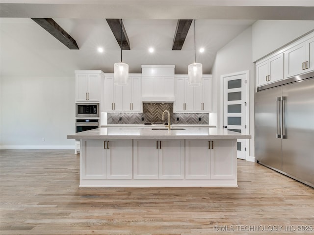 kitchen with white cabinets, an island with sink, built in appliances, light countertops, and backsplash