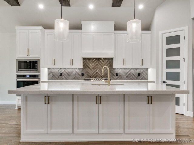 kitchen featuring tasteful backsplash, white cabinetry, stainless steel appliances, and a kitchen island with sink