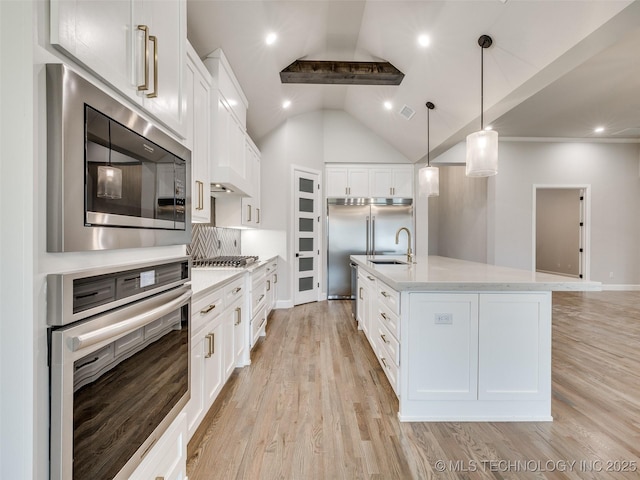 kitchen with a sink, built in appliances, light wood finished floors, white cabinets, and lofted ceiling
