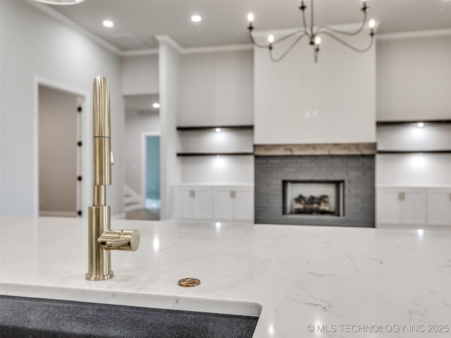 kitchen with a sink, recessed lighting, light stone countertops, a fireplace, and ornamental molding