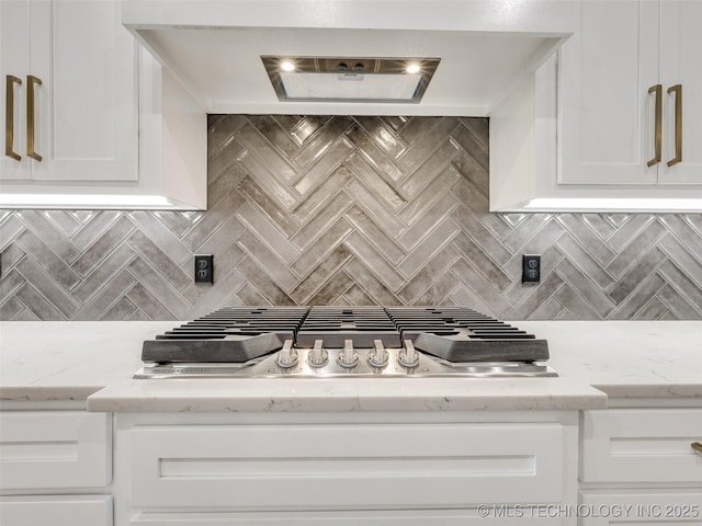 kitchen featuring wall chimney range hood, stainless steel gas cooktop, decorative backsplash, white cabinets, and light stone countertops