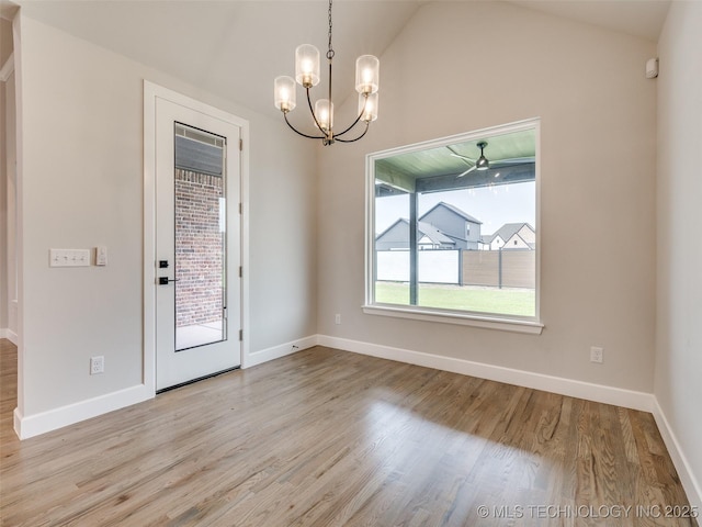 unfurnished dining area featuring baseboards, a notable chandelier, wood finished floors, and lofted ceiling