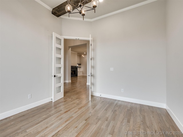 empty room with wood finished floors, baseboards, ornamental molding, and an inviting chandelier