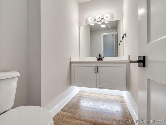 half bath with baseboards, toilet, vanity, and wood finished floors