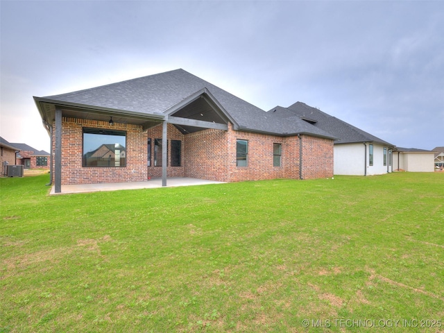 rear view of house with cooling unit, brick siding, a patio, and a lawn