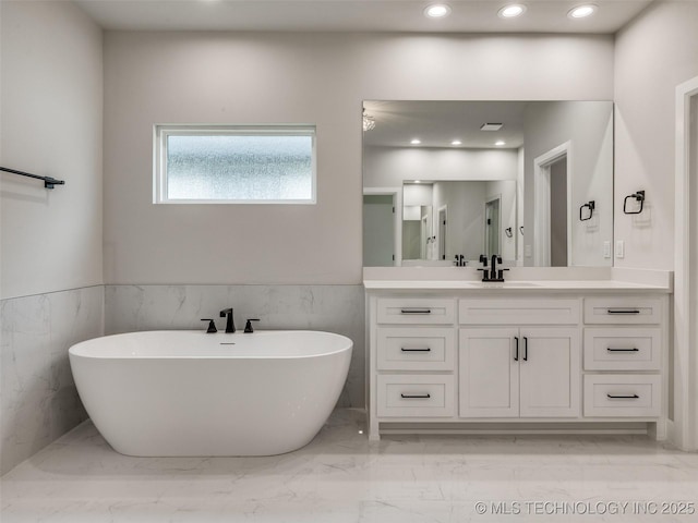 bathroom featuring wainscoting, marble finish floor, a freestanding tub, and vanity