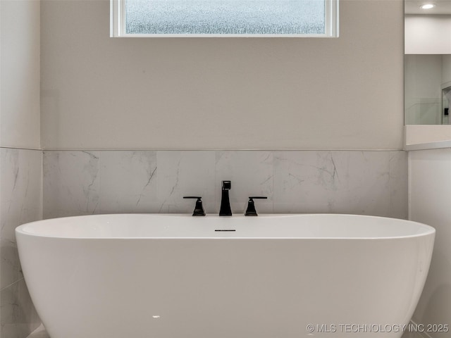 bathroom with a freestanding tub, tile walls, and a healthy amount of sunlight