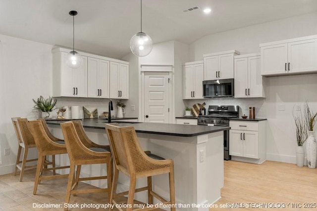 kitchen featuring stainless steel appliances, hanging light fixtures, dark countertops, and white cabinetry