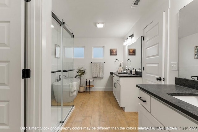 full bathroom with two vanities, wood finished floors, visible vents, a freestanding bath, and a stall shower