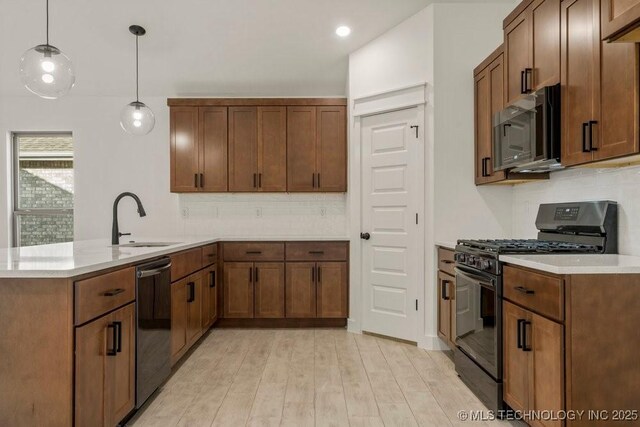 kitchen featuring tasteful backsplash, sink, hanging light fixtures, black appliances, and light wood-type flooring