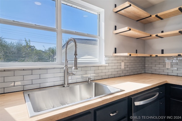 kitchen with wood counters, light wood-type flooring, tasteful backsplash, dishwashing machine, and sink