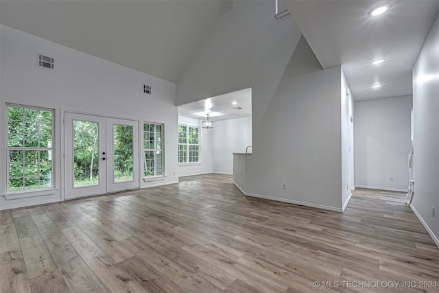 unfurnished living room with light hardwood / wood-style flooring, high vaulted ceiling, french doors, and an inviting chandelier