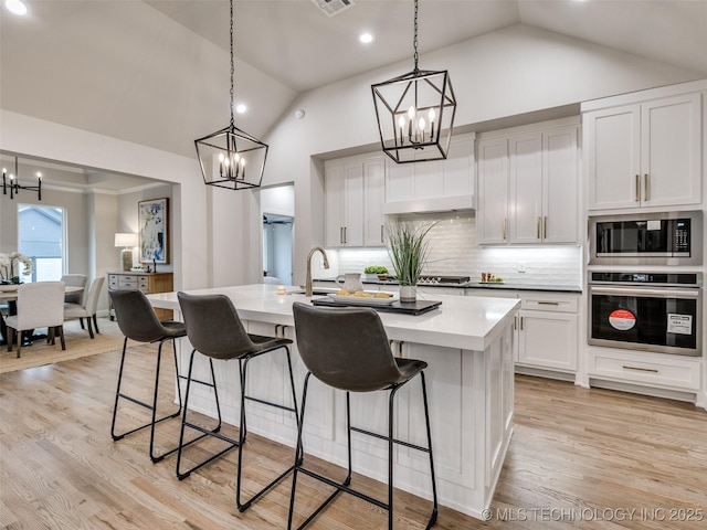 kitchen featuring white cabinetry, stainless steel appliances, decorative light fixtures, and a center island with sink