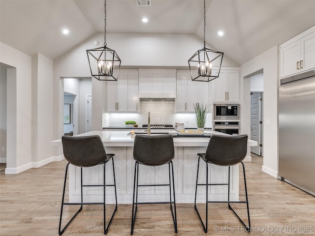 kitchen featuring an island with sink, pendant lighting, built in appliances, and white cabinets