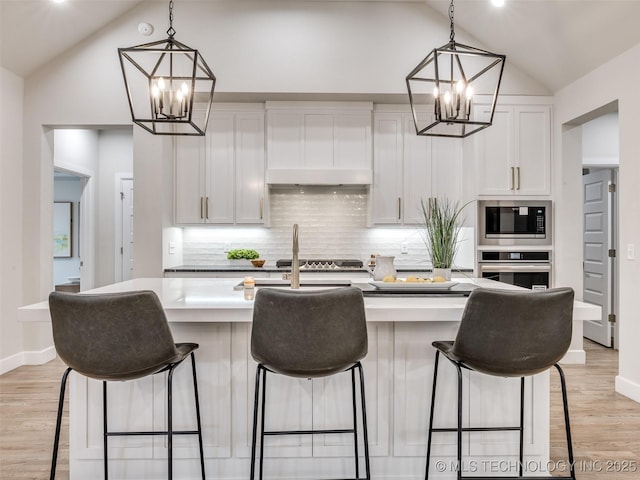 kitchen featuring white cabinetry, appliances with stainless steel finishes, a kitchen island with sink, and decorative light fixtures