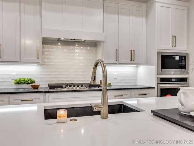 kitchen with dark stone countertops, backsplash, stainless steel appliances, ventilation hood, and white cabinets