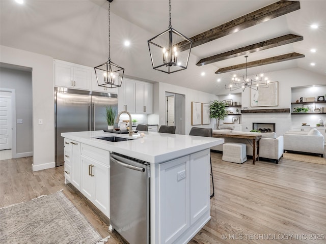 kitchen with sink, a kitchen island with sink, hanging light fixtures, white cabinets, and stainless steel dishwasher