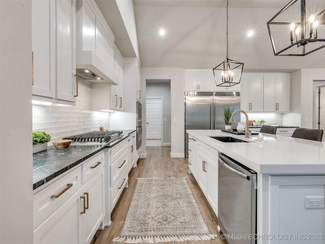 kitchen with stainless steel appliances, hanging light fixtures, a center island with sink, and white cabinets