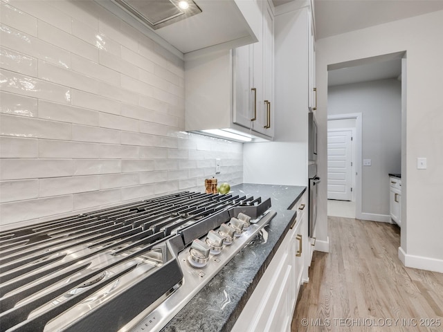 kitchen featuring white cabinets, dark stone counters, decorative backsplash, stainless steel gas cooktop, and light hardwood / wood-style flooring