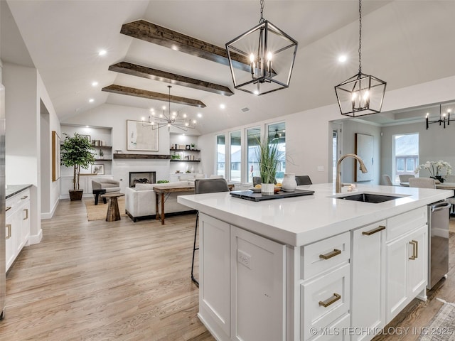 kitchen with sink, a kitchen island with sink, hanging light fixtures, vaulted ceiling with beams, and white cabinets