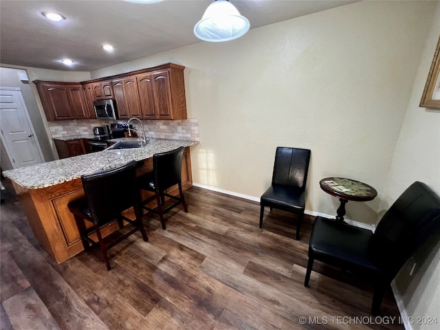 kitchen featuring dark wood-type flooring, stainless steel appliances, kitchen peninsula, a breakfast bar area, and decorative backsplash