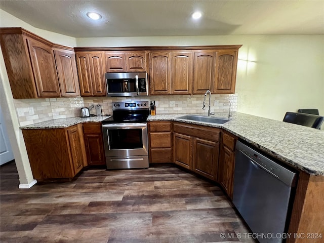 kitchen featuring kitchen peninsula, appliances with stainless steel finishes, dark hardwood / wood-style flooring, decorative backsplash, and sink