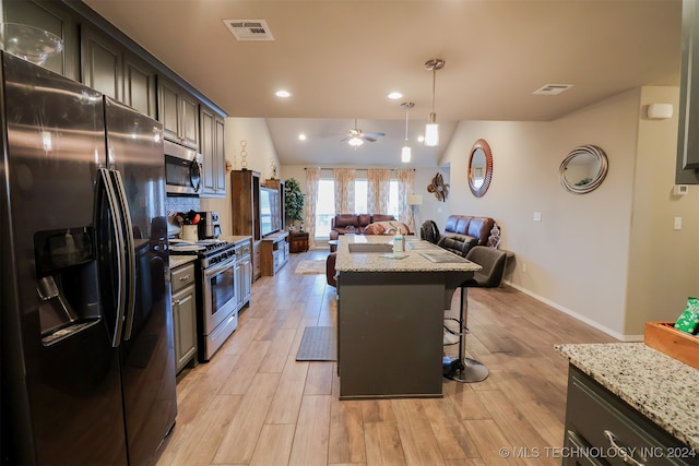 kitchen with light stone countertops, a center island, light hardwood / wood-style flooring, a breakfast bar area, and appliances with stainless steel finishes