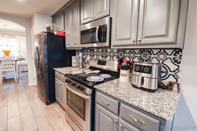 kitchen featuring backsplash, gray cabinets, light stone counters, and stainless steel appliances