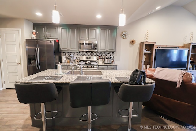 kitchen featuring decorative light fixtures, light stone countertops, stainless steel appliances, and vaulted ceiling