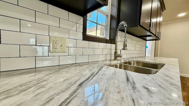 interior details featuring light stone countertops, tasteful backsplash, dark brown cabinets, crown molding, and sink