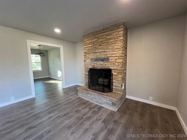 unfurnished living room featuring a stone fireplace, dark wood finished floors, and baseboards