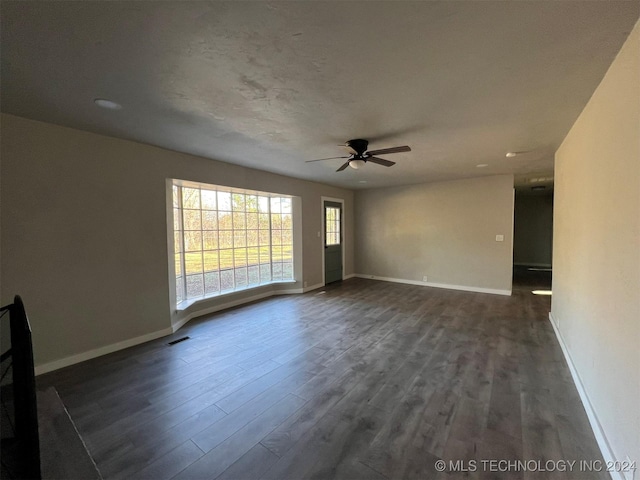 empty room featuring ceiling fan, dark wood finished floors, visible vents, and baseboards