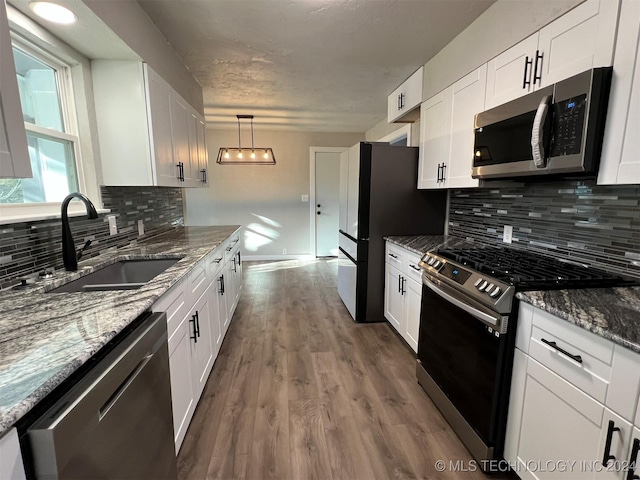 kitchen with stainless steel appliances, a sink, white cabinetry, and decorative light fixtures