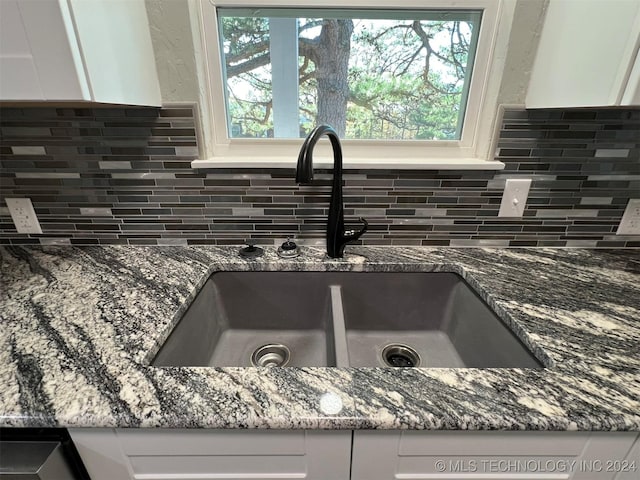 interior details featuring white cabinetry, a sink, and dark stone countertops