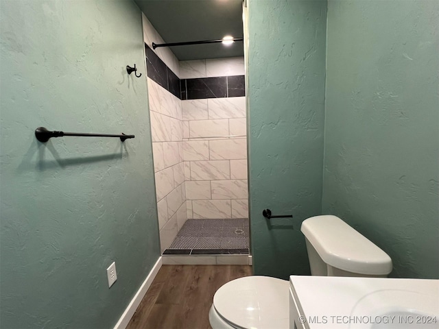 bathroom with baseboards, a textured wall, toilet, wood finished floors, and a shower stall