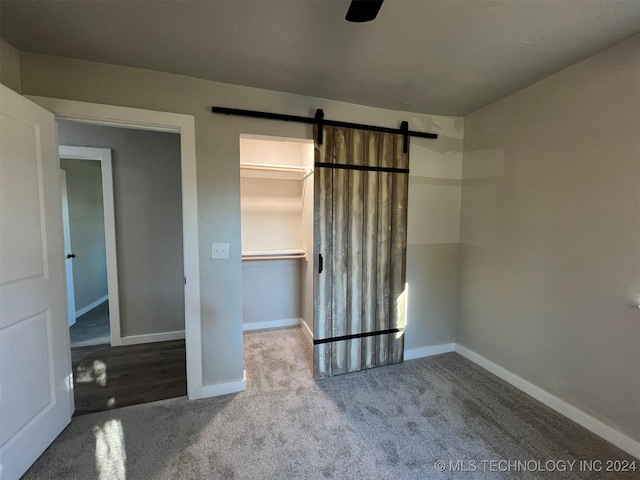 unfurnished bedroom featuring carpet floors, a barn door, a spacious closet, and baseboards