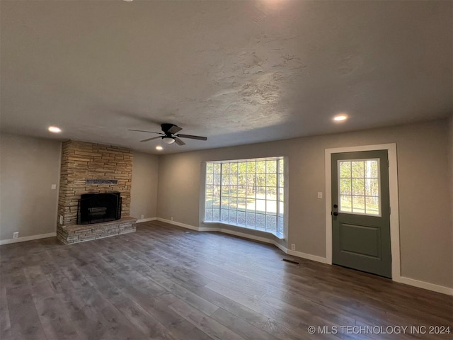 unfurnished living room with a stone fireplace, wood finished floors, visible vents, and baseboards