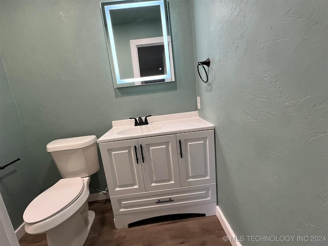 half bath with toilet, a textured wall, vanity, and baseboards