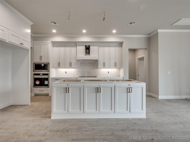 kitchen featuring white cabinetry, a center island with sink, built in microwave, oven, and ornamental molding