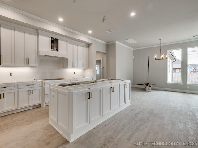 kitchen featuring white cabinetry, a kitchen island with sink, ornamental molding, pendant lighting, and ceiling fan with notable chandelier