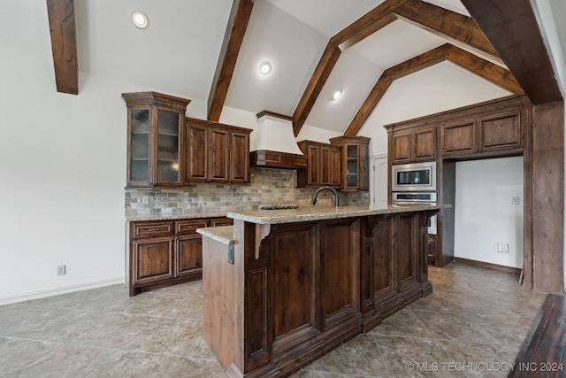 kitchen featuring a kitchen island with sink, vaulted ceiling with beams, decorative backsplash, light stone countertops, and stainless steel appliances